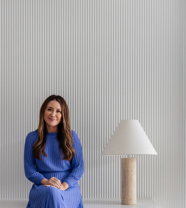 Image of Sharon Hutchings from Arli Homes in a blue dress smiling next to a stylish lamp with white panelling in the background